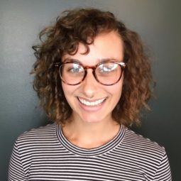 woman wearing glasses and a striped tshirt with shoulder length brunette hair in a curly perm