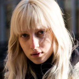 Shot of street style model with long ashy blonde hair and full bangs, wearing winter clothing and posing outside.