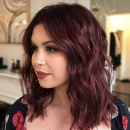 close up shot of woman with mulled wine hair colour, wearing red floral top in a salon