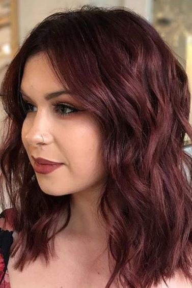 close up shot of woman with mulled wine hair colour, wearing red floral top in a salon