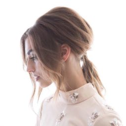 Elegant updos: side view of woman with light brown medium length straight hair styled into a '60s-inspired Bardot ponytail with long bardot bangs