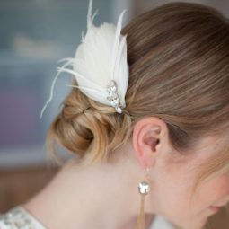 blonde bride with halterneck white dress and a bun hairstyle with feather accessory