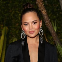 updo hairstyles for work: close up shot of chrissy teigen with braided top knot hairstyle on the red carpet, wearing all black