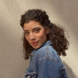 Woman with shoulder length medium natural curls styled into a half up style