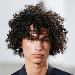 male model on the runway with dark brown curly hair worn long and loose