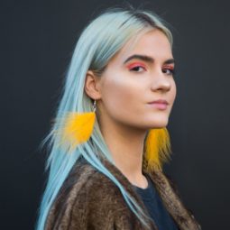 Does dyeing your hair damage it: Woman with sky blue hair, wearing yellow fluffy earrings with furry jacket posing for a street style shot