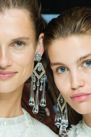 hair shine spray: close up shot of two women with shine spray, wearing earrings and white sparkly dress