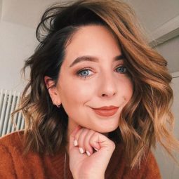 Fall hair colours: Zoe Sugg Zoella with a cinnamon wavy bob wearing a brown jumper resting her chin on her hand.