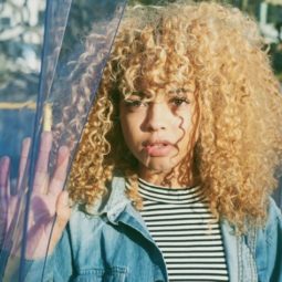 blonde natural haired woman with a full fringe wearing a denim jacket and striped tshirt