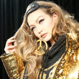 How to get thicker hair: Backstage shot of Gigi Hadid at the Moschino X H&M fashion show, with voluminous wavy blonde hair, wearing a gold puffa jacket