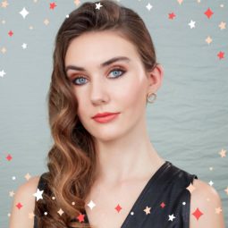 Party hair tips: Woman with chestnut brown glam hollywood curls, wearing black and posing against a grey background in a studio setting