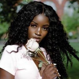 close up shot of woman with long mermaid curly weave hairstyle, wearing white rose and a pink top, posing outside