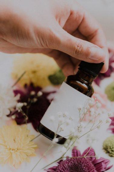 Hand holding a brown bottle in front of a bowl of flowers