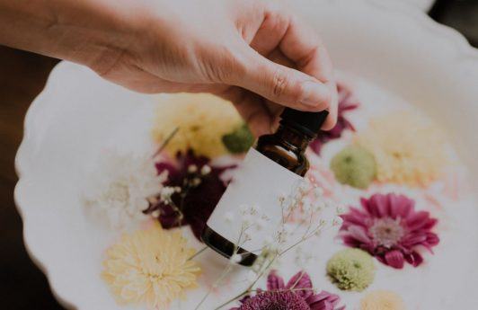 Hand holding a brown bottle in front of a bowl of flowers