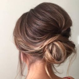 back view of a woman with light brown and dirty blonde straight hair in a low updo with bouffant volume at the crown