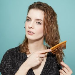 woman with shoulder-length brown-blonde curly hair using a wide tooth comb to gently brush through it