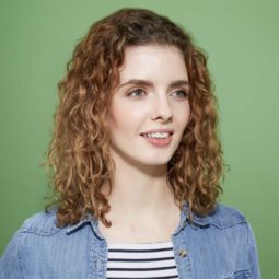 How to scrunch hair tutorial: Woman with brown curly shoulder length hair wearing a striped top and denim shirt