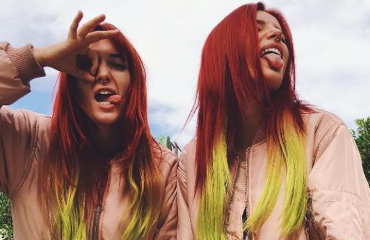 Bella with twin sister Dani Thorne posing wearing pink jackets and long straight hair dyed in a red to yellow ombre