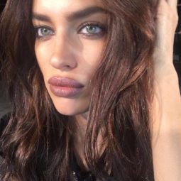 Irina Shayk with long brown hair worn in undone waves touching her hair