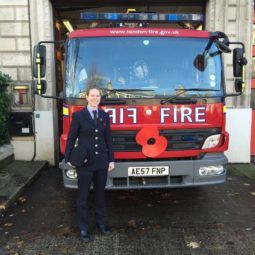 Working It: Woman with blonde hair in a bun updo standing in front of afire engine.