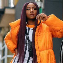 best hair colour for black women: close up shot of black woman with long purple hair, wearing orange jacket and stripped white shirt