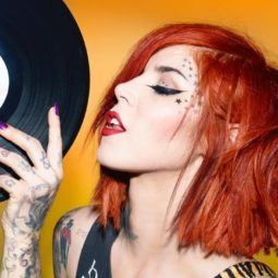 kat von d with dyed red hair holding a vinyl record with purple nails and stars on her face