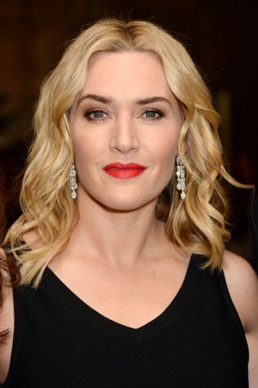 kate winslet in a black v neck dress with shoulder length blonde wavy hair