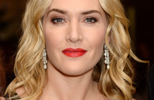 kate winslet in a black v neck dress with shoulder length blonde wavy hair