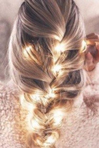 blonde woman in bed with her hair in a thick french braid with fairy lights