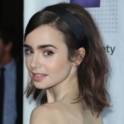 lily collins wearing a strapless black dress with her brunette hair in a bouffant style with a black headband