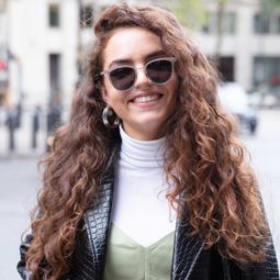 Long curly hair: Close up shot of a woman with long chestnut brown curly hair, wearing black jacket and jumper and posing outside