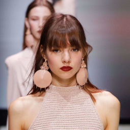 woman on the runway with a long fringe hairstyle wearing a pastel pink outfit