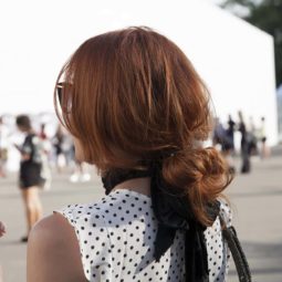 Updos for long hair: Model with brown hair in low messy bun hairstyle with a large black bow ribbon and spotted top