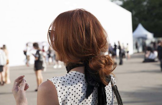 Updos for long hair: Model with brown hair in low messy bun hairstyle with a large black bow ribbon and spotted top