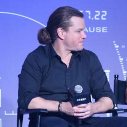 image of matt damon sat down holding a microphone with his long brown hair worn in a low man bun