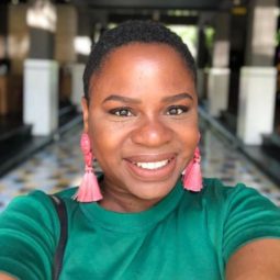 Real Hair Stories Nadia Williams: Young black woman with shaved hairstyles wearing a green top and statement earrings