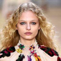 a curly female fashion model wearing floral shirt walking on the runway