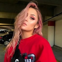 girl with pastel rose gold hair wearing a red sweatshirt with a black supreme bum bag