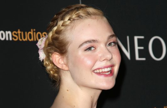 Elle Fanning with her golden blonde hair styled into a braided crown updo with floral clips in it