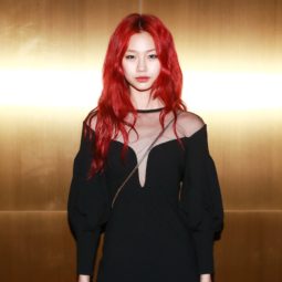 Close up shot of model with red hair, wearing black dress and posing against golden wall