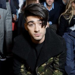 zayn malik sat down wearing a black and khaki coat with his dark brown hair worn in a side fringe