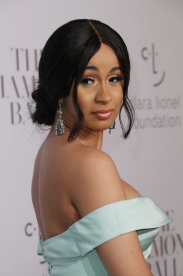 Cardi B looking over shoulder with black hair in low updo with loose strands framing the face wearing strapless blue dress