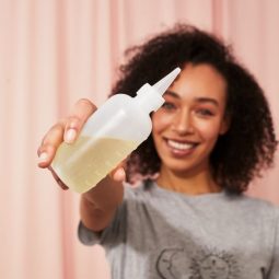 Woman with naturally curly short hair holding a bottle of oil