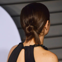 work hairstyles for long hair: back view of charli XCX with medium dark brown hair styled in a low twisted bun on red carpet