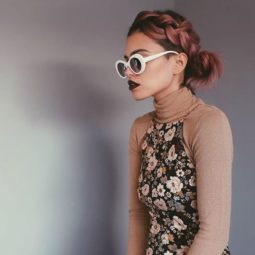 side view of woman with short metallic pink red hair styled with a headband braid secured into a side bun