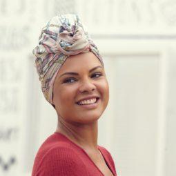 woman with naturally curly brown hair wearing a silk scarf in a twisted knot wearing a pink red top