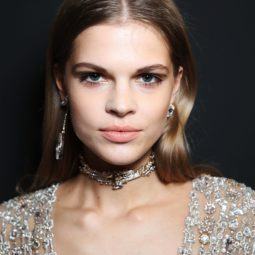 prom hairstyles: close up shot of model with polished waves hair, wearing glittery gown and neck choker, backstage at a show