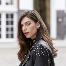 Thicker hair products: Close up shot of woman with loose curly brown hair, wearing a leather jacket and tassel earrings and posing outside