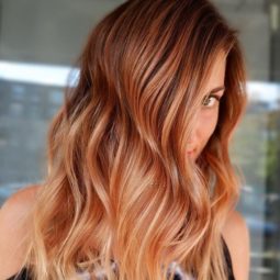 Spiced cider hair: Woman with long, wavy spiced cider pumpkin hair, wearing black and posing in a salon