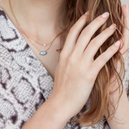 Shampoo for split ends product guide: Close up shot a woman holding her with medium copper wavy hair, wearing a snake print top and an eye of Horus necklace, in a studio